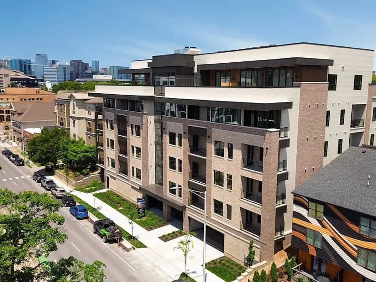This image features a modern apartment building surrounded by lush greenery, with the urban skyline visible in the background. The scene captures both the contemporary design of the property and its connection to the city, hinting at proximity to business districts and convenient urban living.