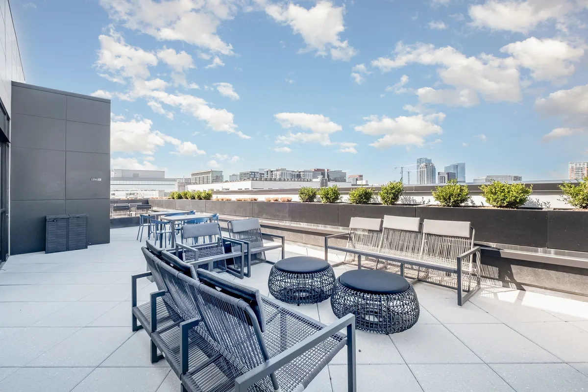 The image showcases a chic rooftop seating area adorned with lush planters, offering sweeping sunset views of the Nashville city skyline. The scene exudes a relaxed, contemporary vibe, ideal for casual gatherings or unwinding after a day exploring Music Row.