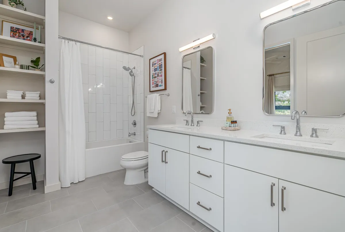 A modern bathroom with a double sink vanity, a shower area, and shelves neatly arranged with fresh towels, creating a bright, fresh, and functional space.