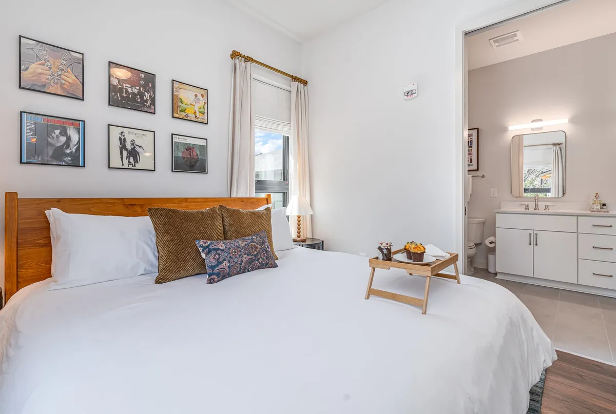 A comfortable bedroom scene with a bed dressed in decorative pillows, artwork on the walls, and a nightstand with a lamp, creating a peaceful, home-like atmosphere.