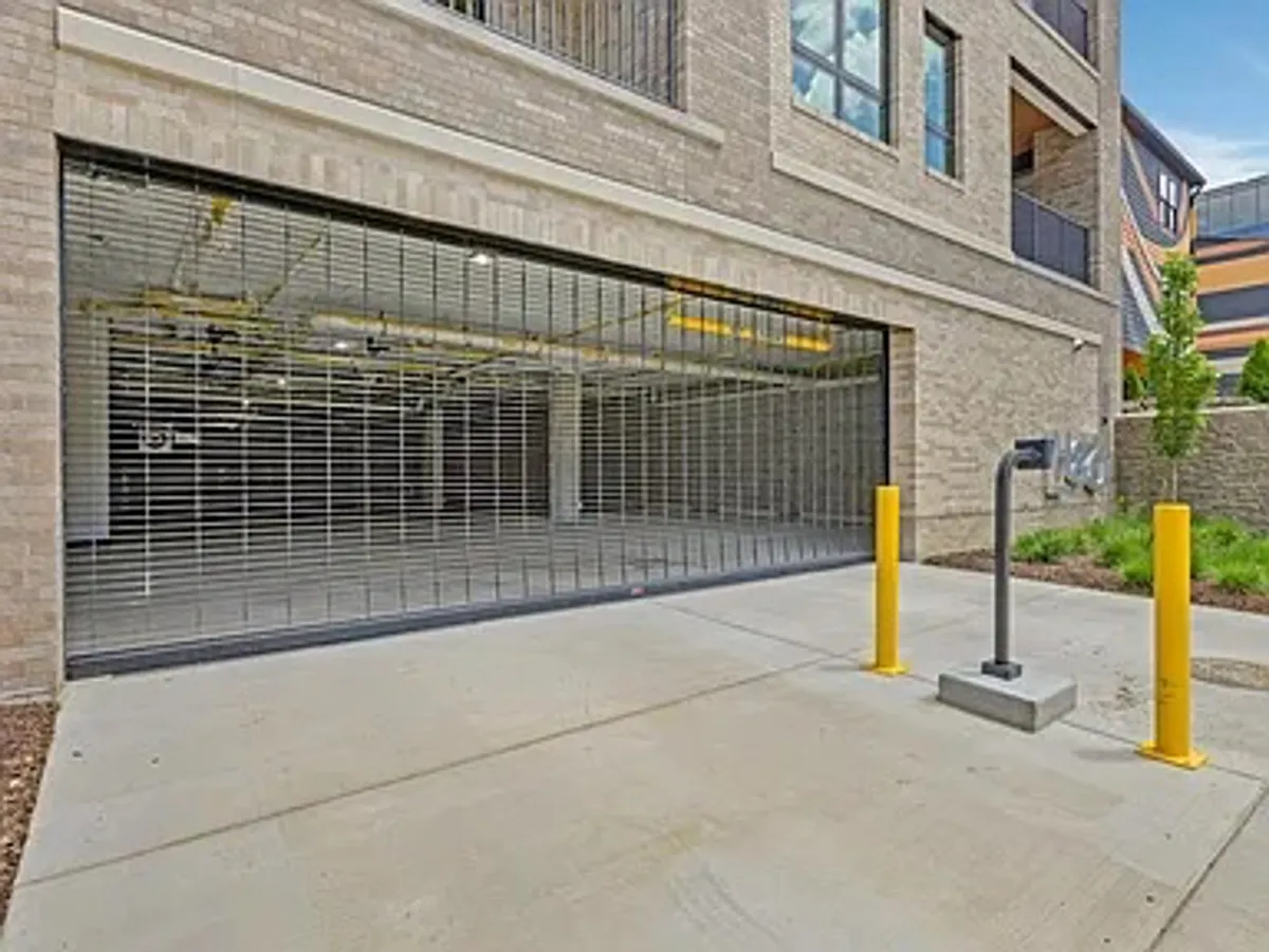 A secure garage entrance with a prominent security gate and yellow bollards, signaling organized and safe parking for residents. The design is clean and modern, underlining convenience and peace of mind.